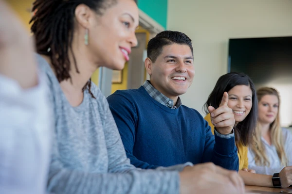 A diverse group of four people sitting at a table, engaging in a lively discussion with smiles and attentive expressions.