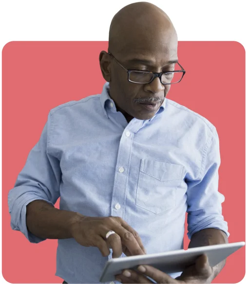 Man wearing glasses and a blue shirt uses a tablet against a solid pink background.