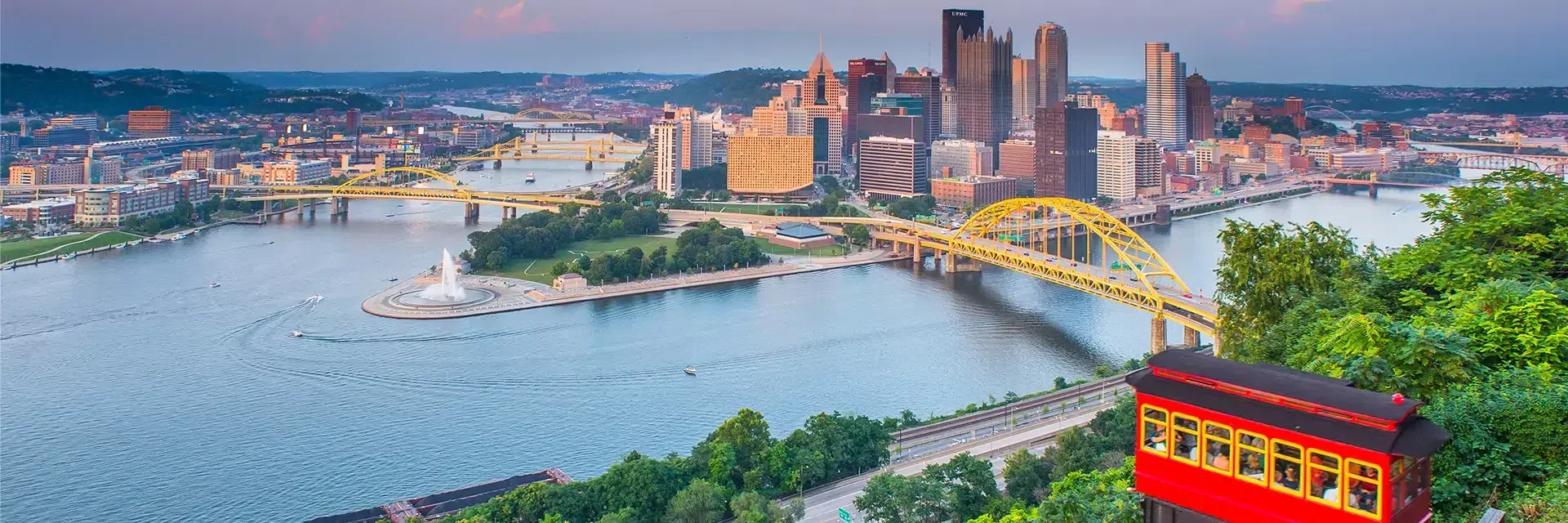 City skyline with yellow bridges over rivers, a fountain, and a red incline car in the foreground, Pittsburgh, PA.